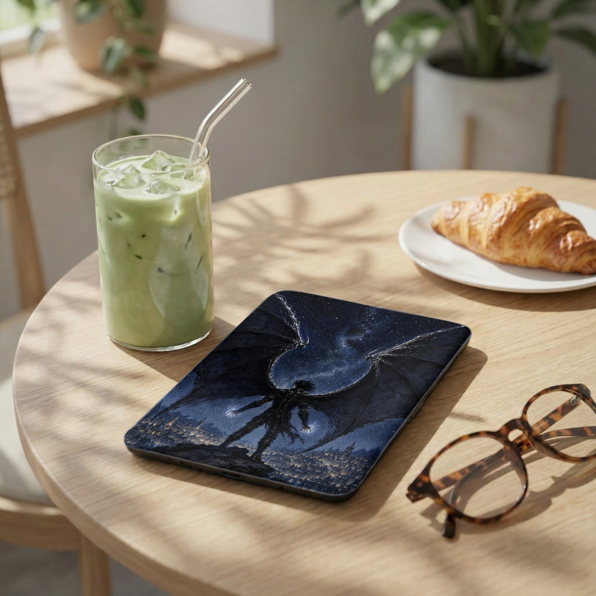 Tablet case with a dragon design on a wooden table next to a drink and croissant.