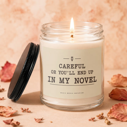 Glass candle with lit wick and black lid, reads "Careful or you'll end up in my novel".