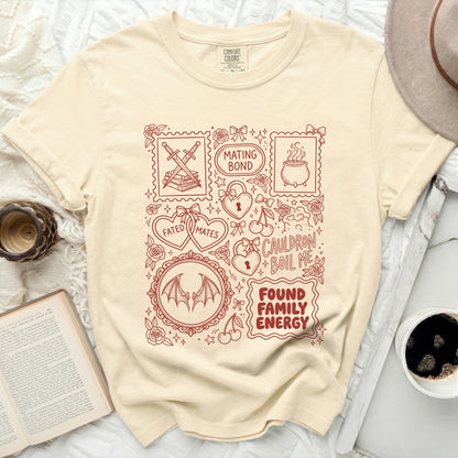 Cream t-shirt with red line art graphics of swords, books, cauldron, heart lock, bats, and text.