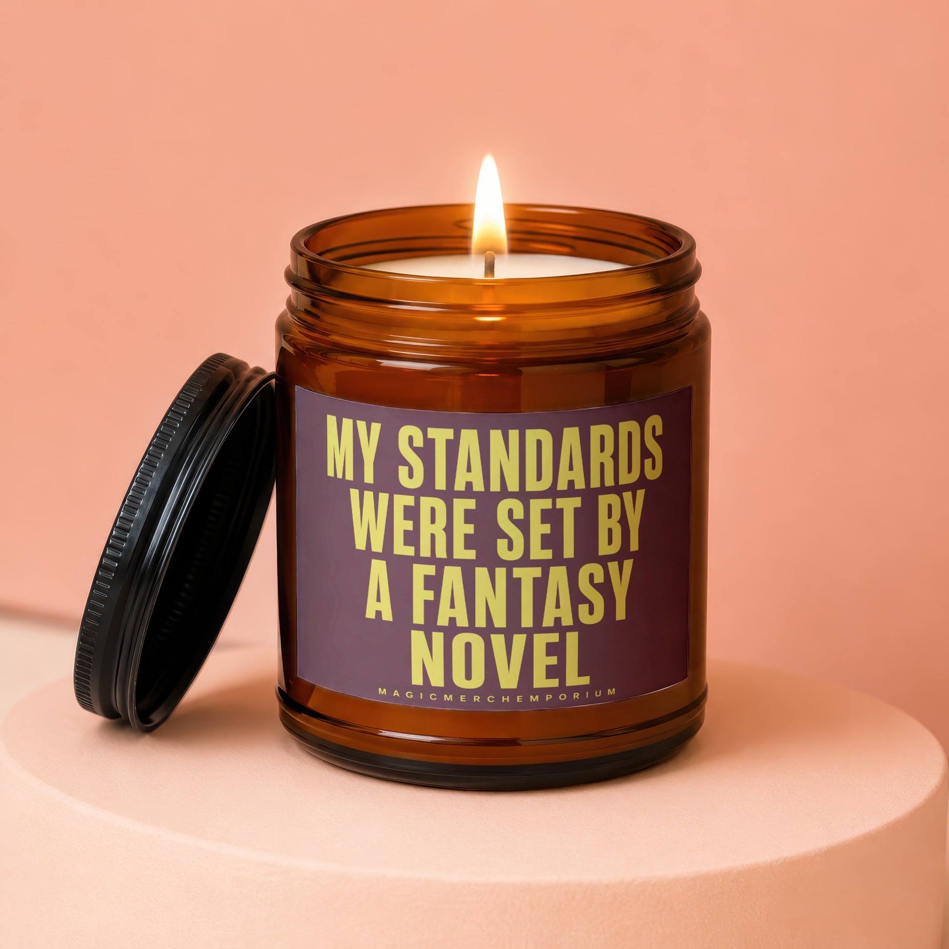 Amber glass candle with lit wick and purple label reading "MY STANDARDS WERE SET BY A FANTASY NOVEL".