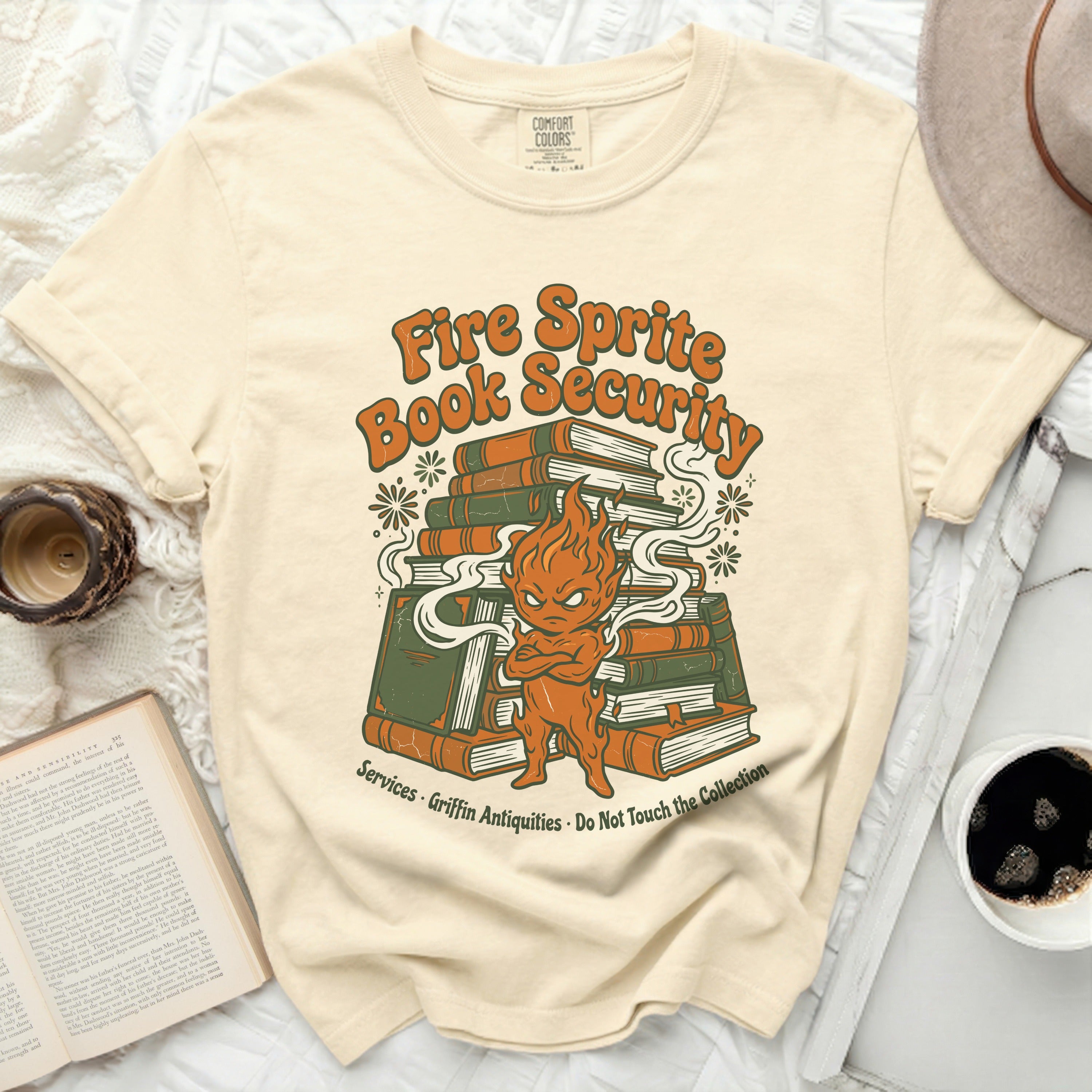Yellow t-shirt with a cartoon fire sprite guarding a stack of books.