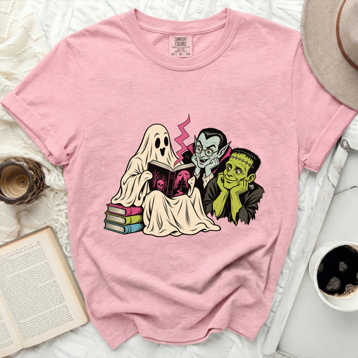Pink t-shirt with a graphic of a ghost, vampire, and Frankenstein reading a book.