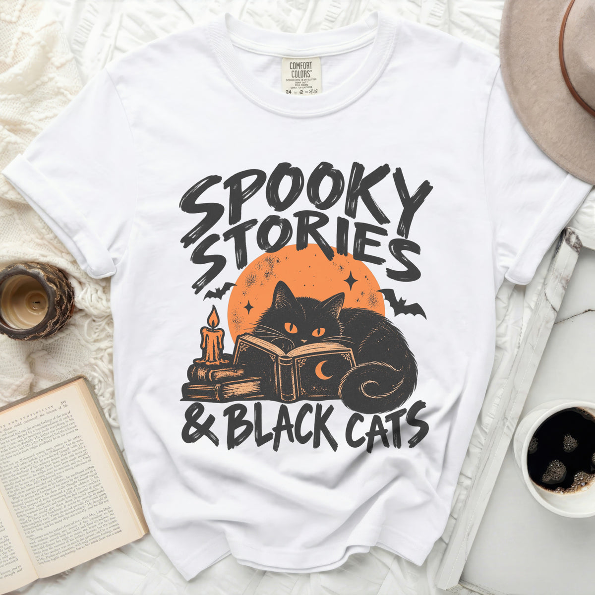 White t-shirt with "Spooky Stories & Black Cats" graphic featuring a black cat reading.