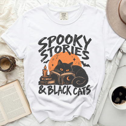 White t-shirt with "Spooky Stories & Black Cats" graphic featuring a black cat reading.