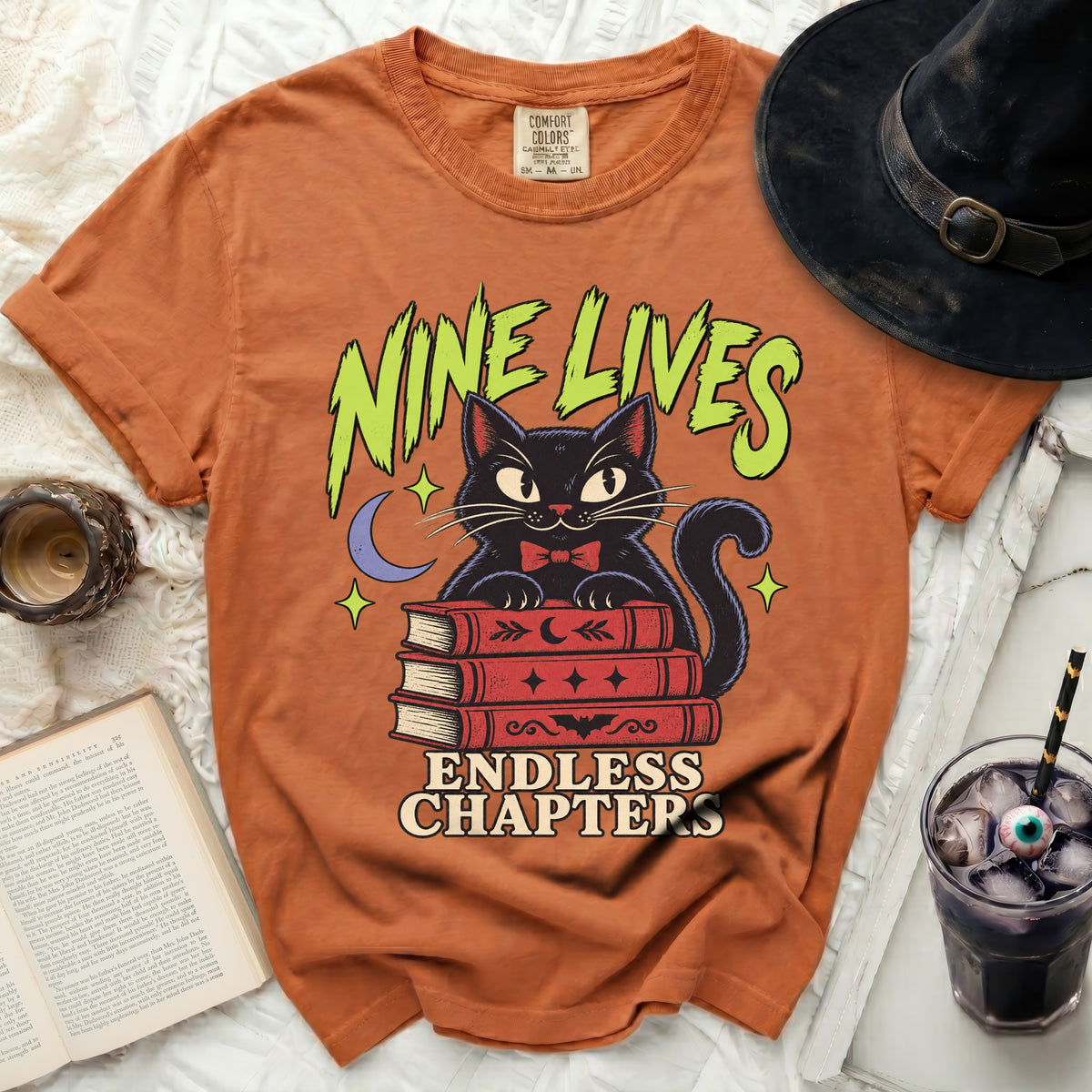 Orange t-shirt with black cat on books, "Nine Lives Endless Chapters" text