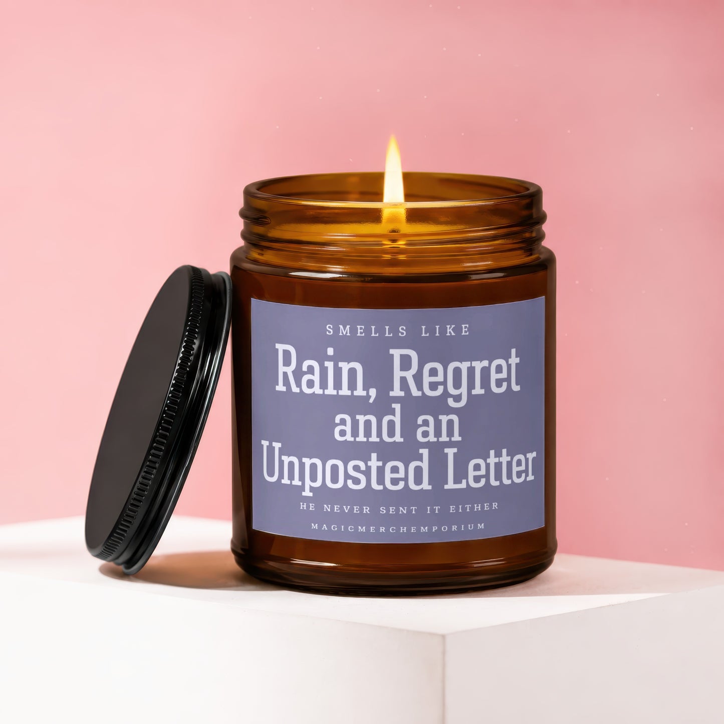 Amber candle with lit flame, black lid, says "Smells Like Rain, Regret and an Unposted Letter."