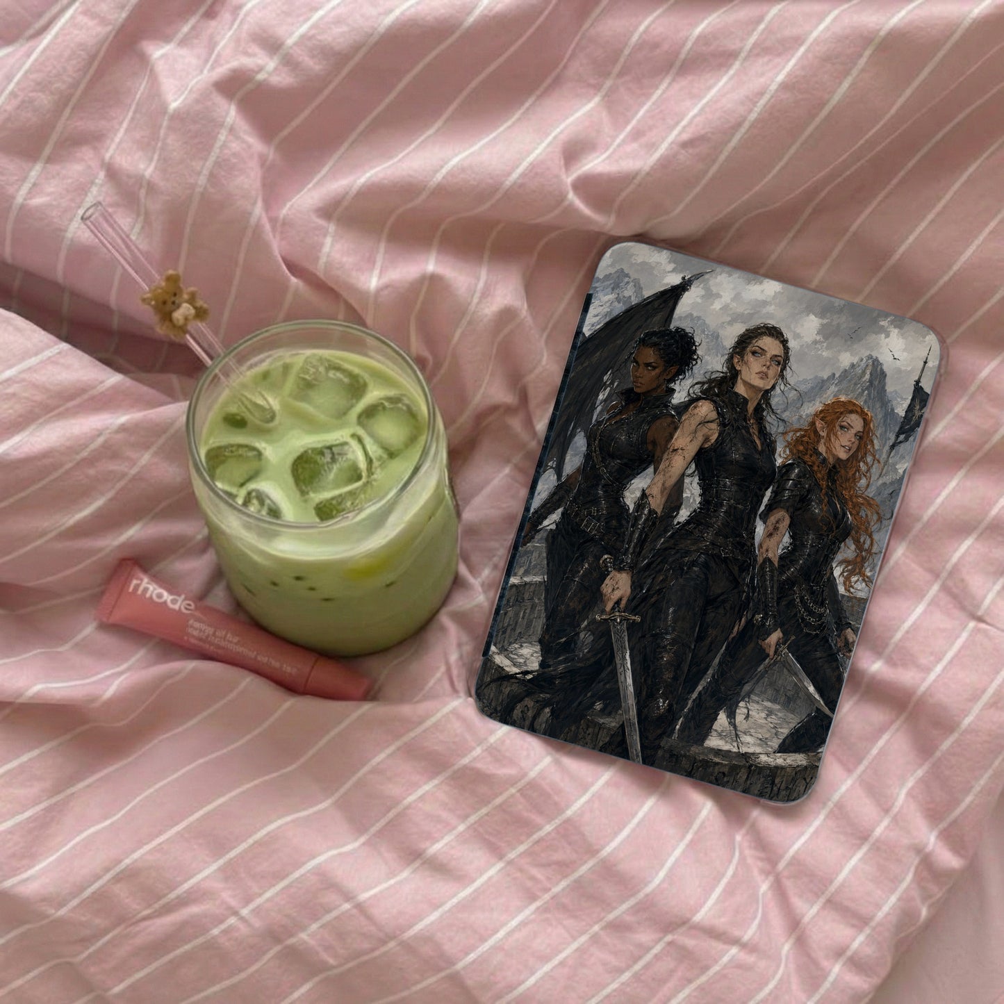 Phone case with three fantasy women in armor, beside green drink and lip balm.