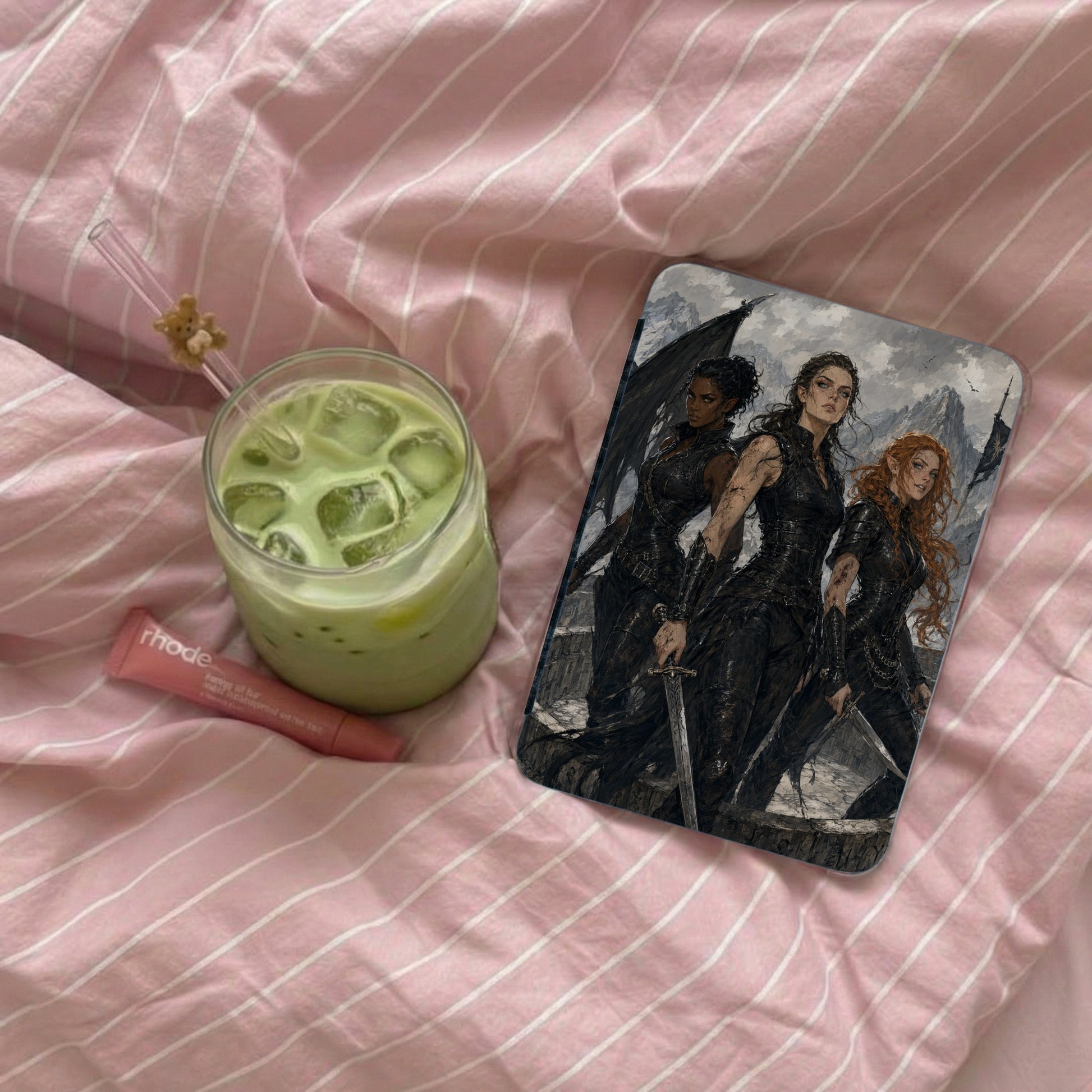 Phone case with three fantasy women in armor, beside green drink and lip balm.