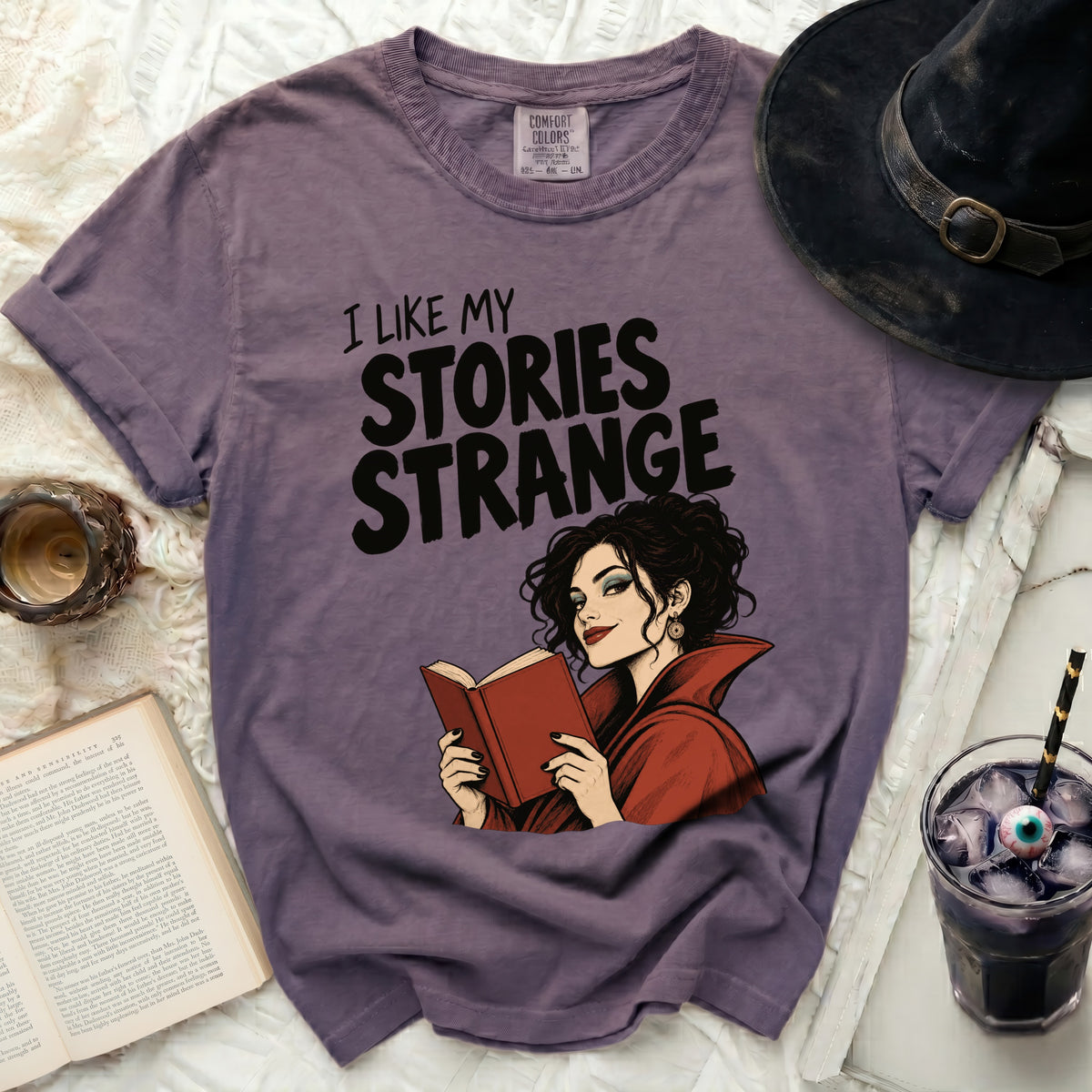 Purple t-shirt with "I LIKE MY STORIES STRANGE" and witch reading book graphic.