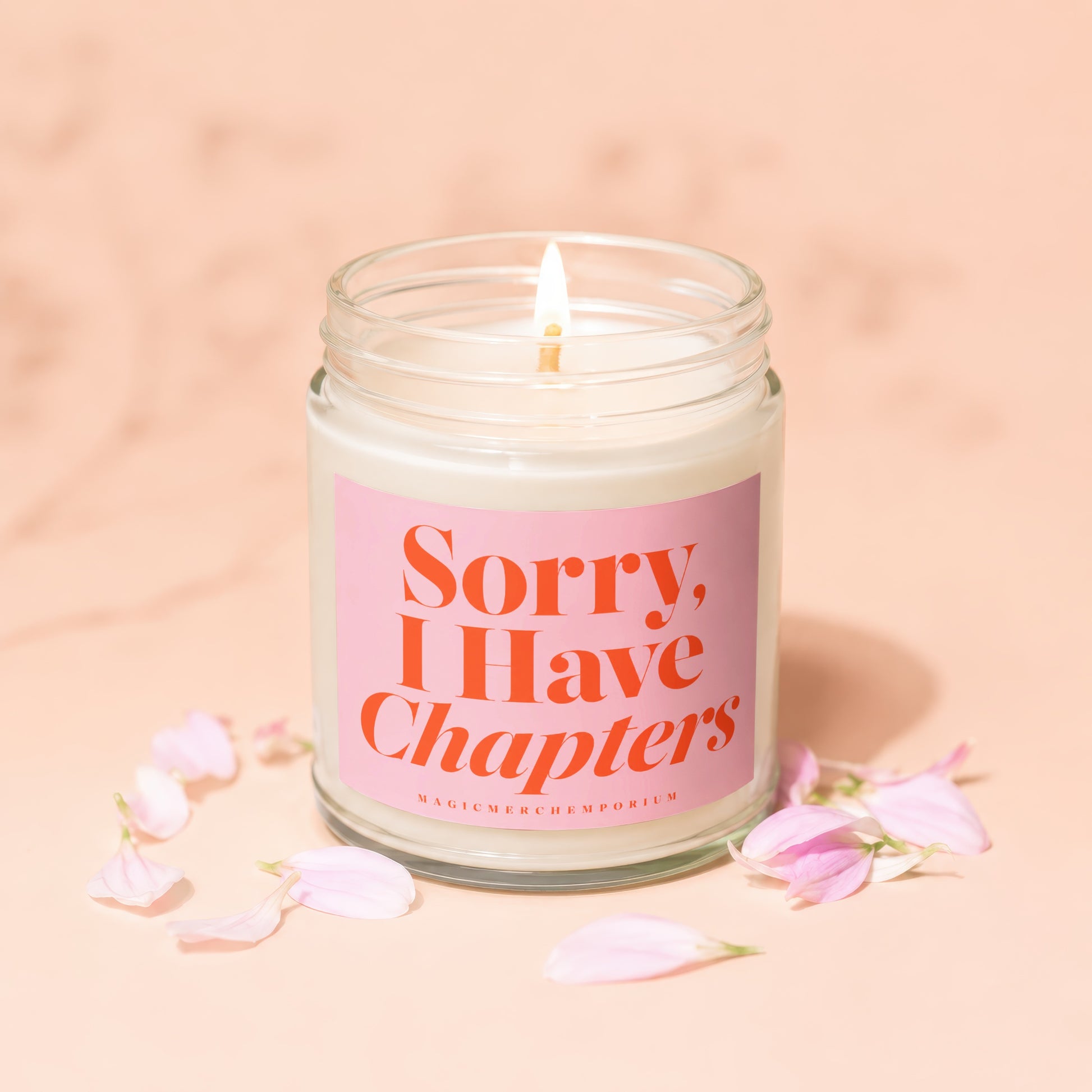 Jar candle with lit wick, pink label reading "Sorry, I Have Chapters".