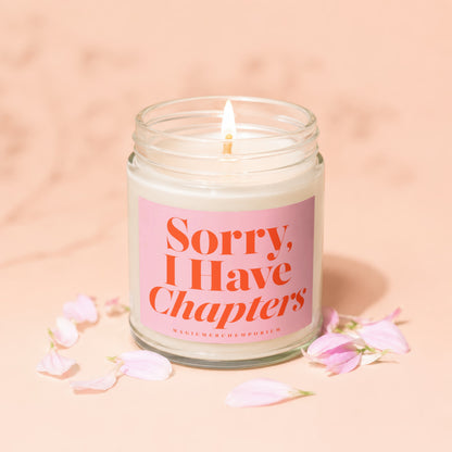 Jar candle with lit wick, pink label reading "Sorry, I Have Chapters".