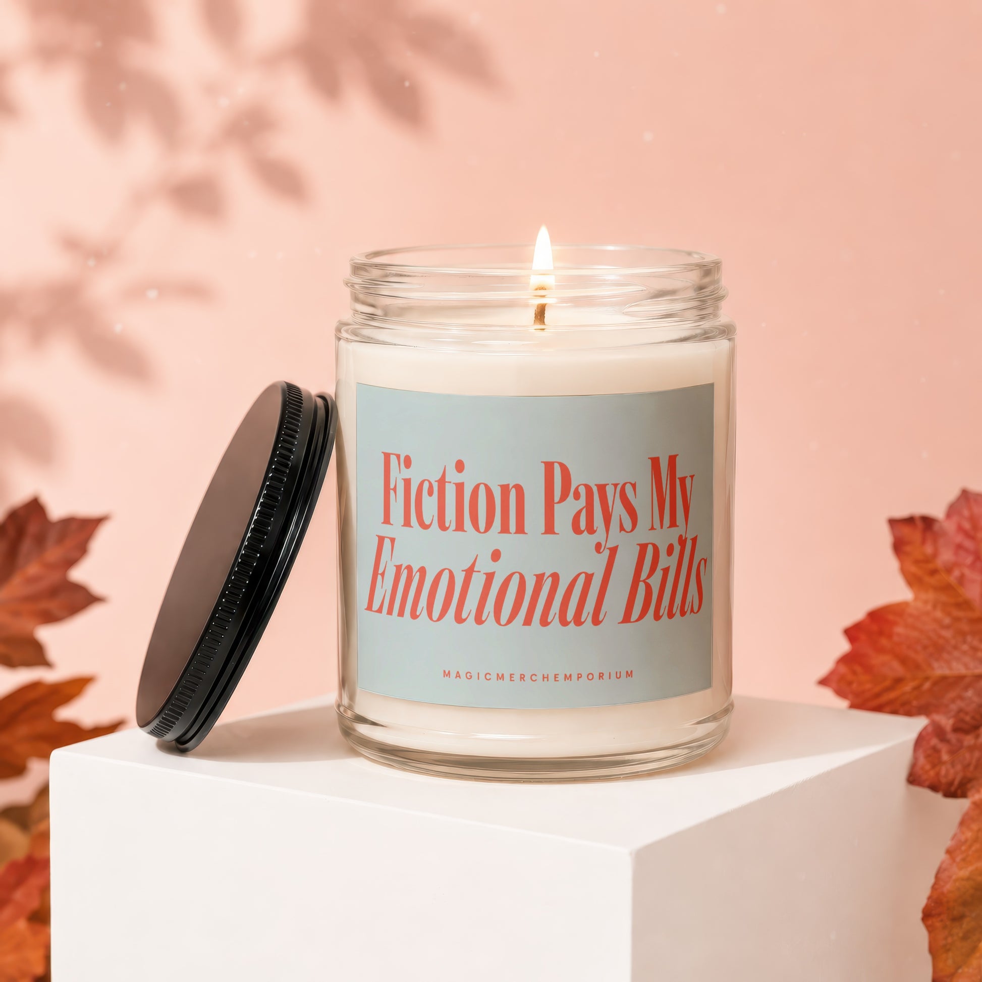Lit glass candle with "Fiction Pays My Emotional Bills" text on pale blue label.