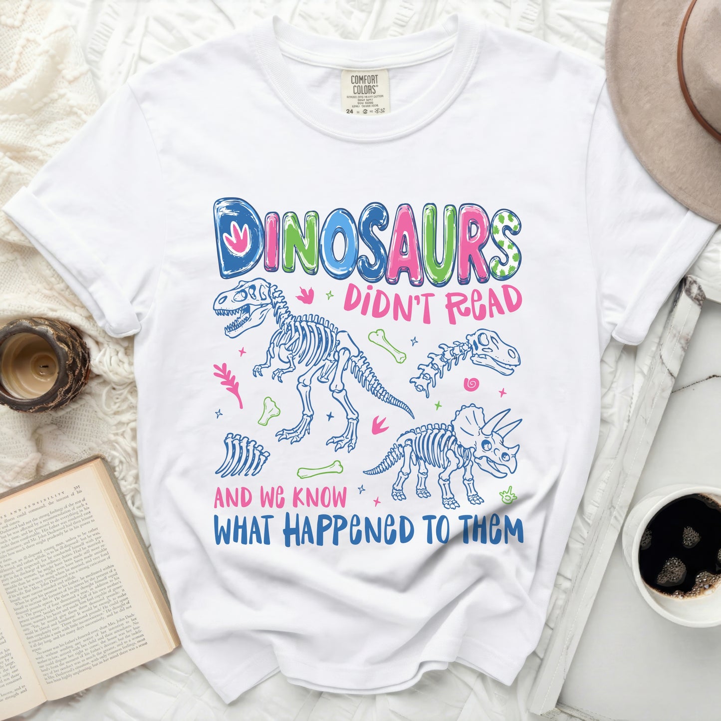 White t-shirt with "Dinosaurs Didn't Read And We Know What Happened To Them" graphic.