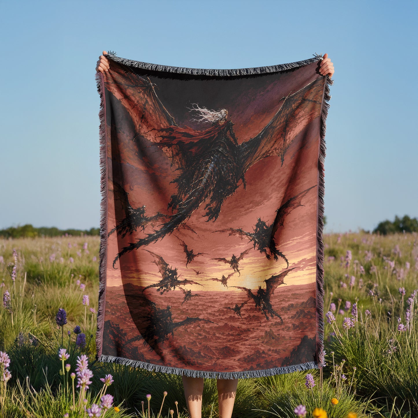 A person is holding up a large blanket with a dragon design on it, standing in a field with purple flowers.