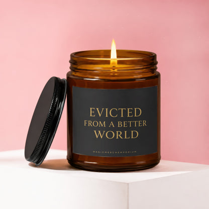 Amber candle with lit wick, black lid, and label reading "Evicted From a Better World".