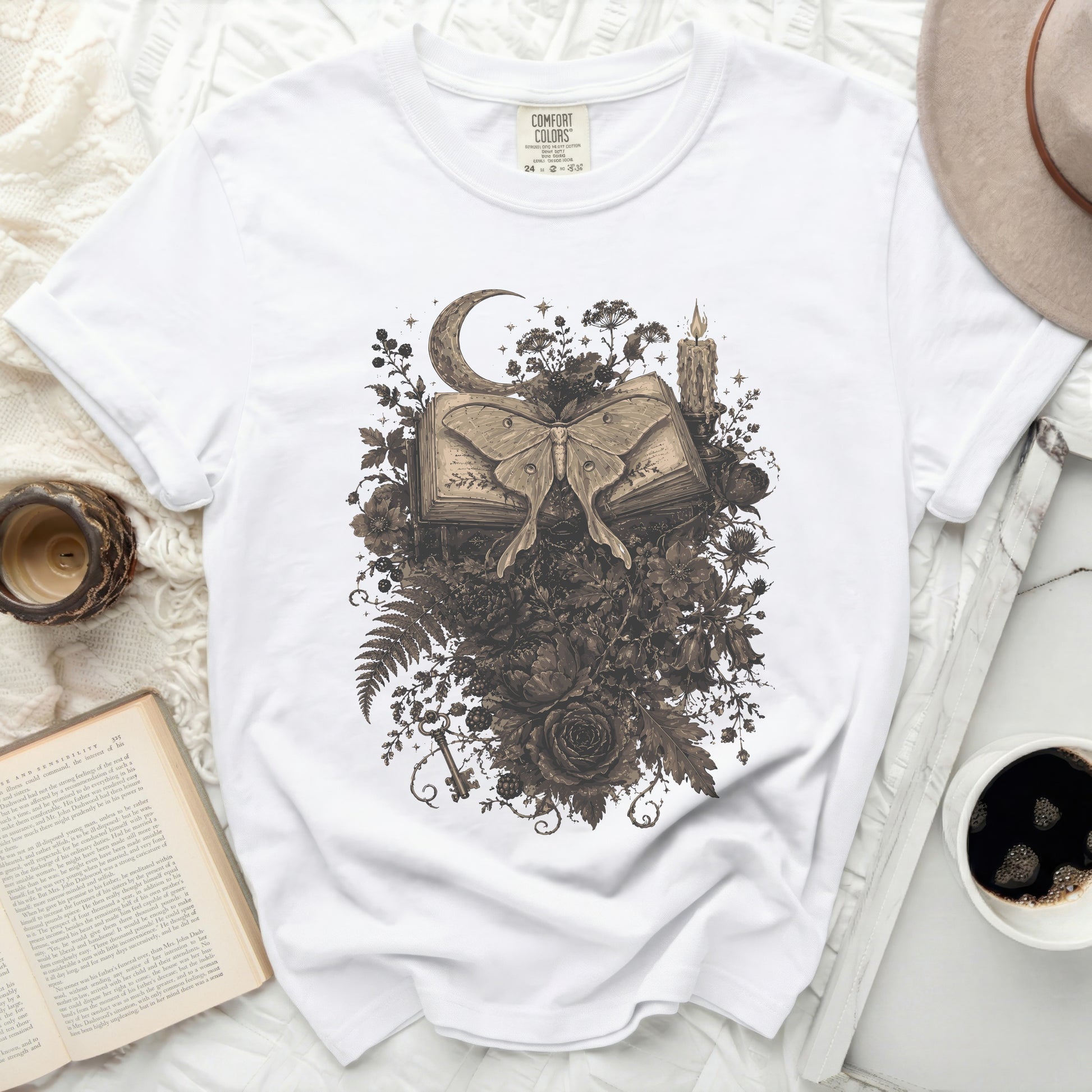 White t-shirt with a vintage moth, book, moon, and floral graphic.