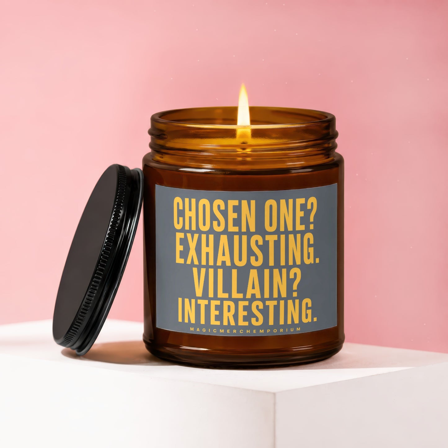 Amber candle with lit flame and lid off, featuring text "CHOSEN ONE? EXHAUSTING. VILLAIN? INTERESTING."