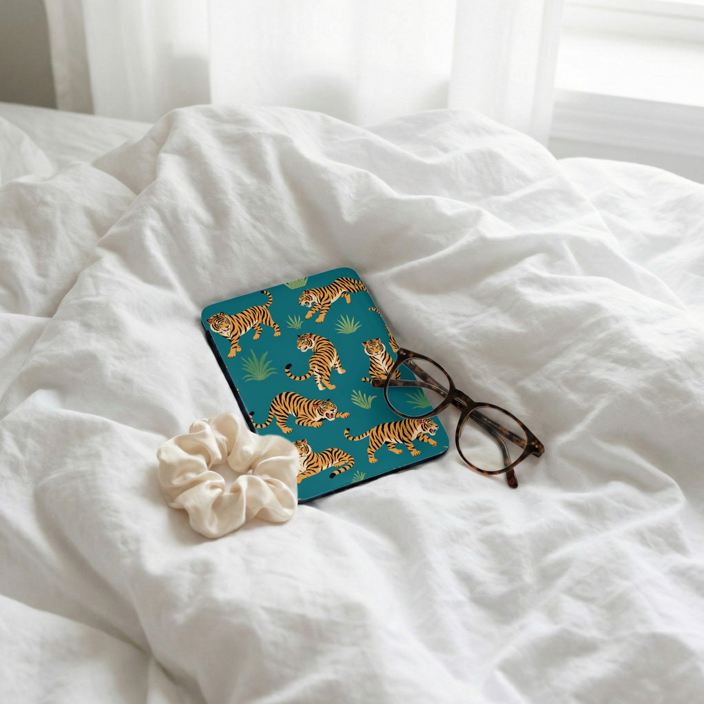 Turquoise case with tiger pattern and eyeglasses on a white textured bed.