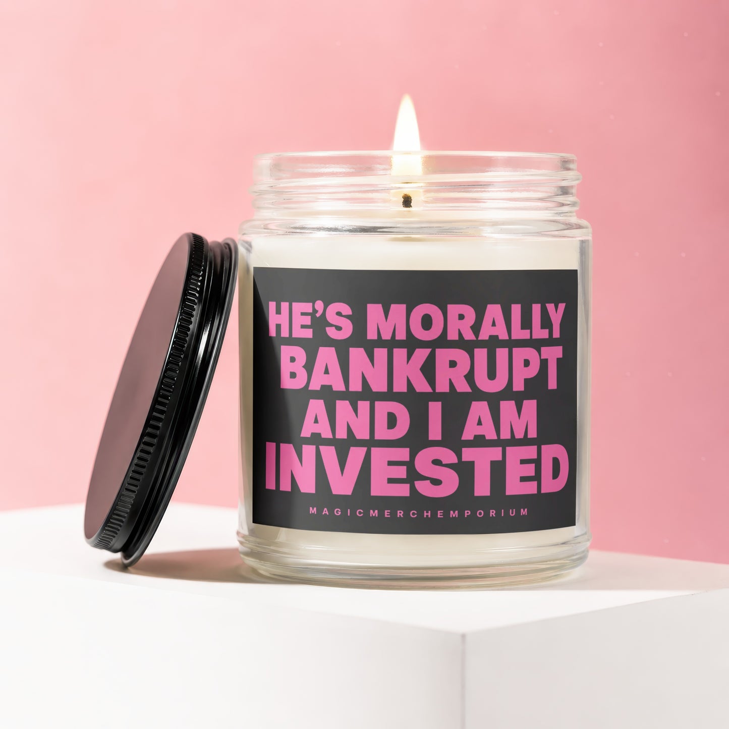 Jar candle with pink text "HE'S MORALLY BANKRUPT AND I AM INVESTED."