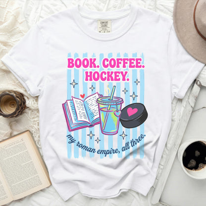 White t-shirt with book, coffee, and hockey puck graphic and text.