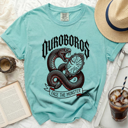 Teal crewneck t-shirt featuring a graphic of a snake, mirror, and the text OUROBOROS FACE THE MONSTER.