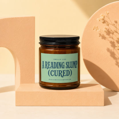 Amber jar candle labeled "A Reading Slump (Cured)" on a peach pedestal.