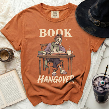 Orange t-shirt with skeleton reading a book and text "BOOK HANGOVER".