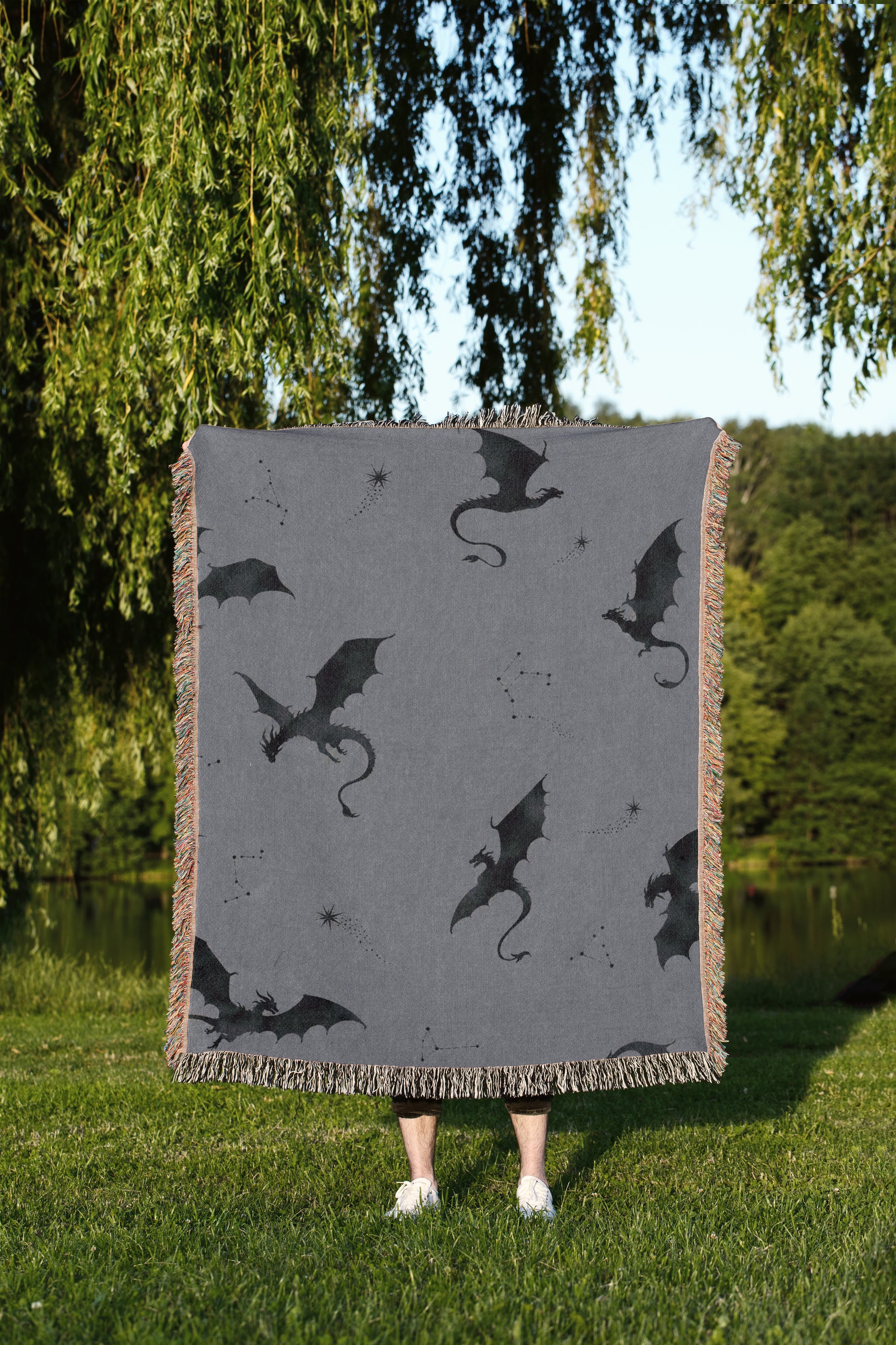 A person is standing in a grassy area, holding a square blanket with a dragon design on it.