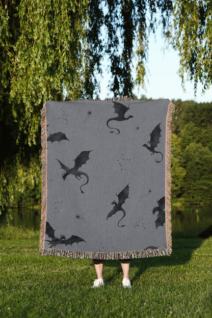A person is standing in a grassy area, holding a square blanket with a dragon design on it.