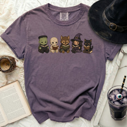 Purple t-shirt with Frankenstein, mummy, werewolf, witch, and cat reading books.