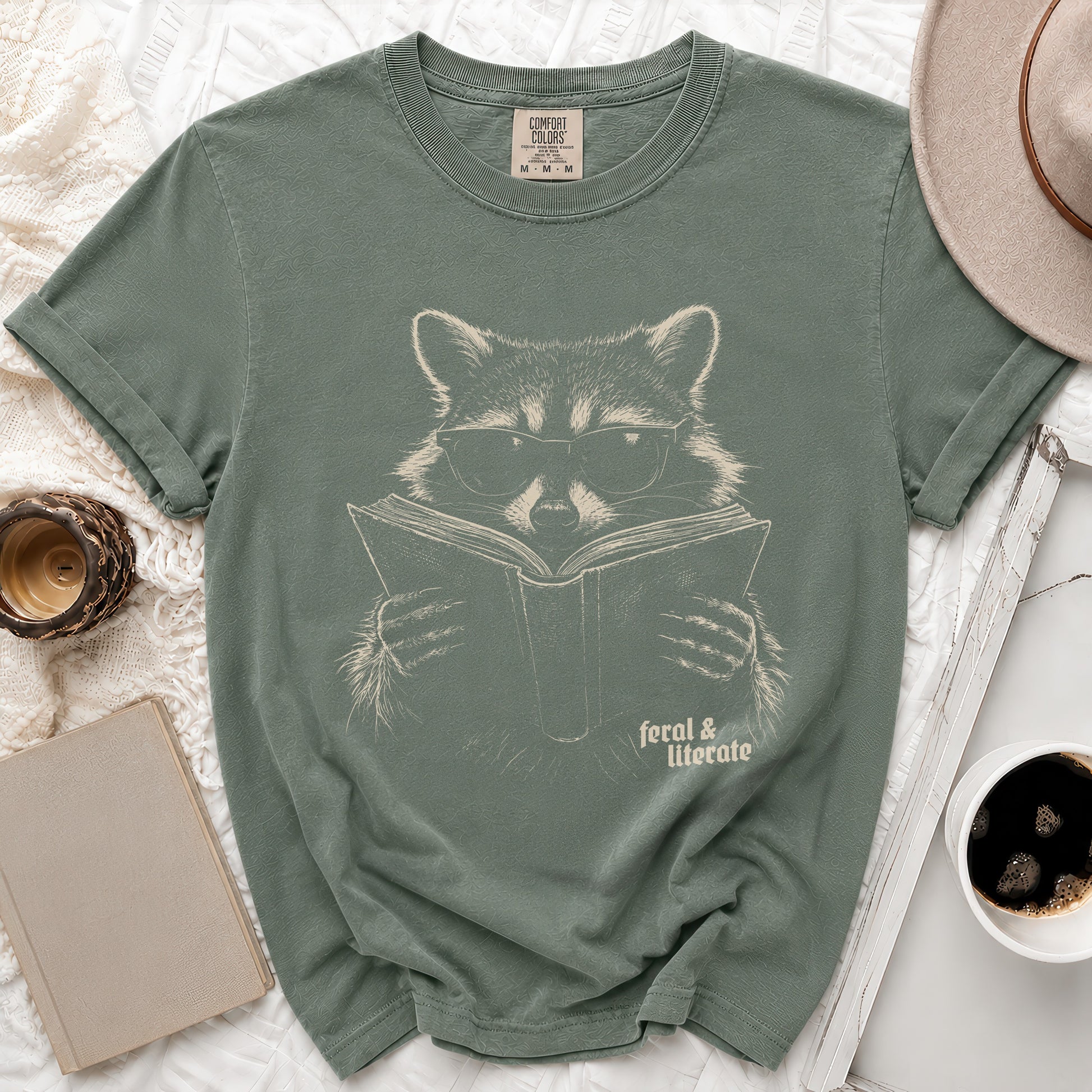 Green t-shirt with a graphic of a raccoon wearing glasses reading a book, "feral & literate" text.