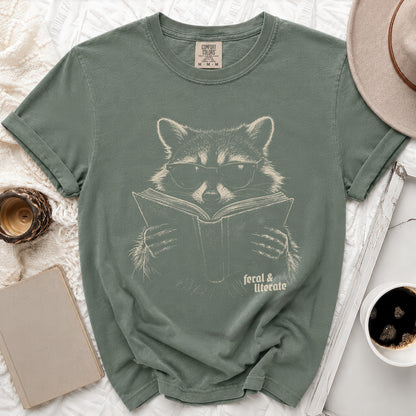Green t-shirt with a graphic of a raccoon wearing glasses reading a book, "feral & literate" text.
