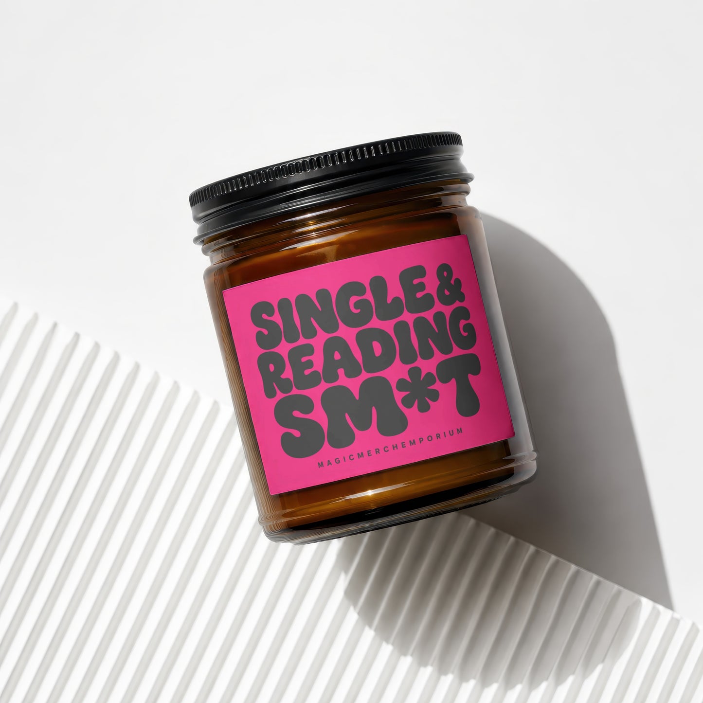 Brown glass candle with pink label reading "Single & Reading Sm*t".
