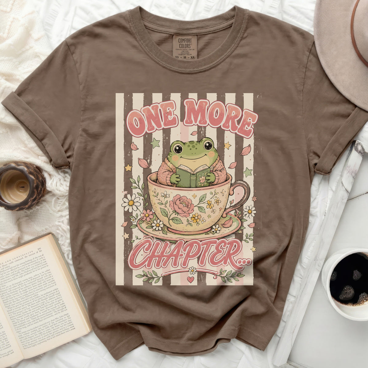 Brown t-shirt with a frog reading in a teacup and "ONE MORE CHAPTER" text.