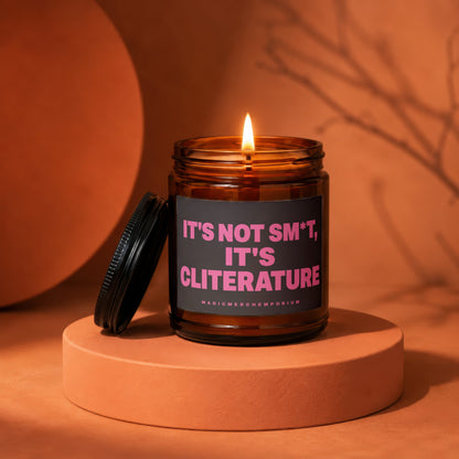 Amber jar candle with lit wick and black lid, reading "IT'S NOT SM*T, IT'S CLITERATURE".