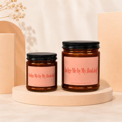 Two brown glass candles with pink labels reading "Judge Me by My Bookshelf."