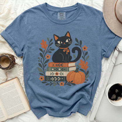 Blue t-shirt with black cat on books, pumpkin, and fall leaves graphic.