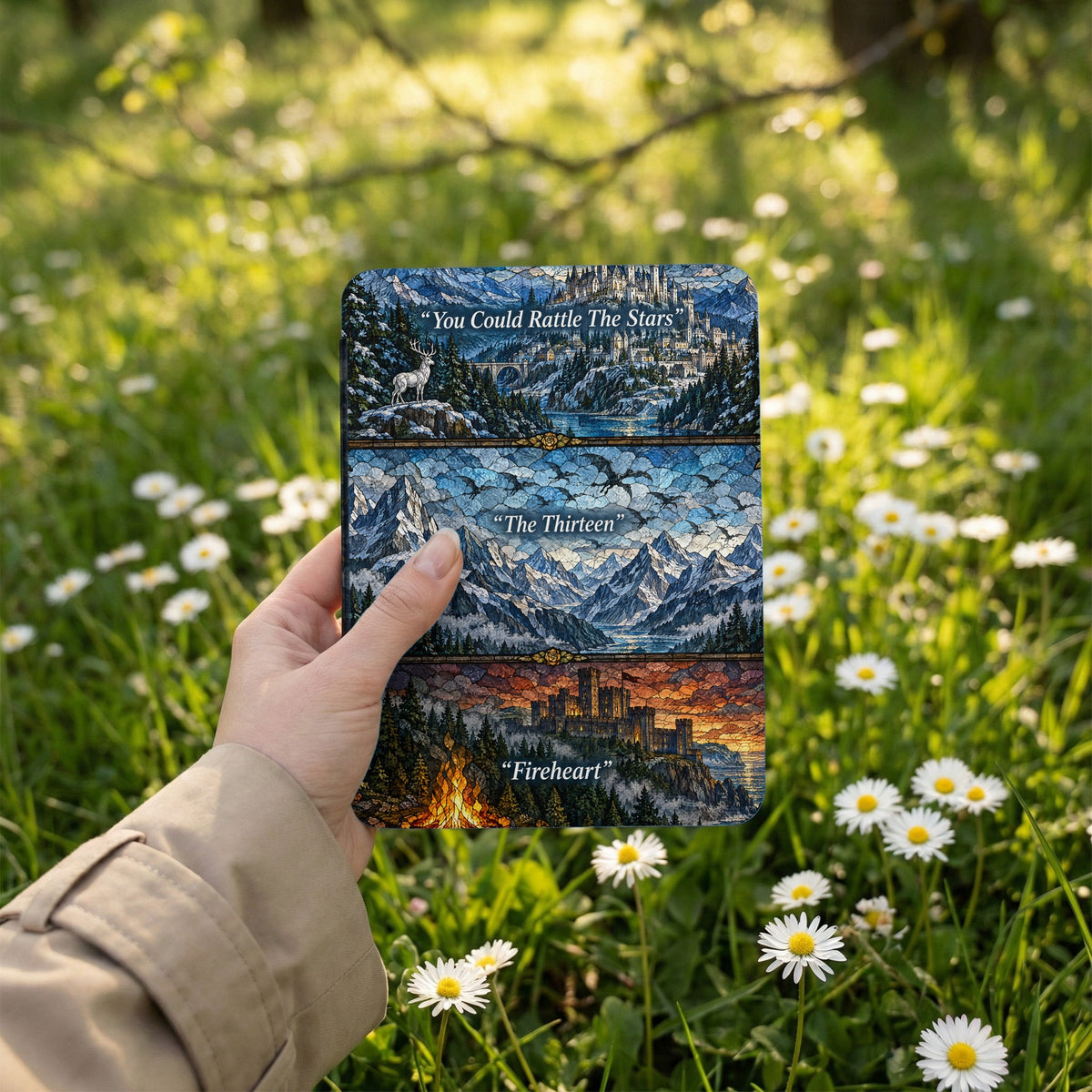 A person holds an e-reader with a stained glass-style fantasy art cover amidst a sunlit field of daisies.