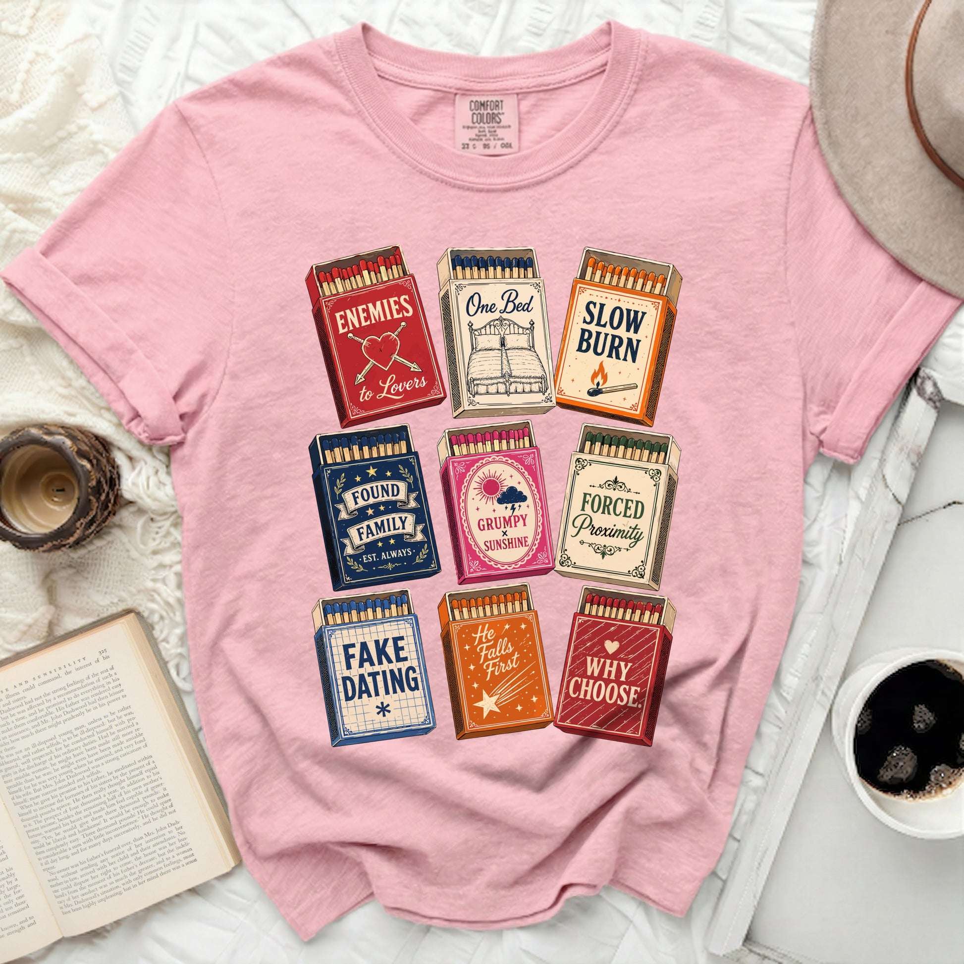 Pink t-shirt with matchbox designs featuring phrases like "One Bed" and "Enemies to Lovers".