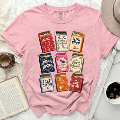 Pink t-shirt with matchbox designs featuring phrases like "One Bed" and "Enemies to Lovers".