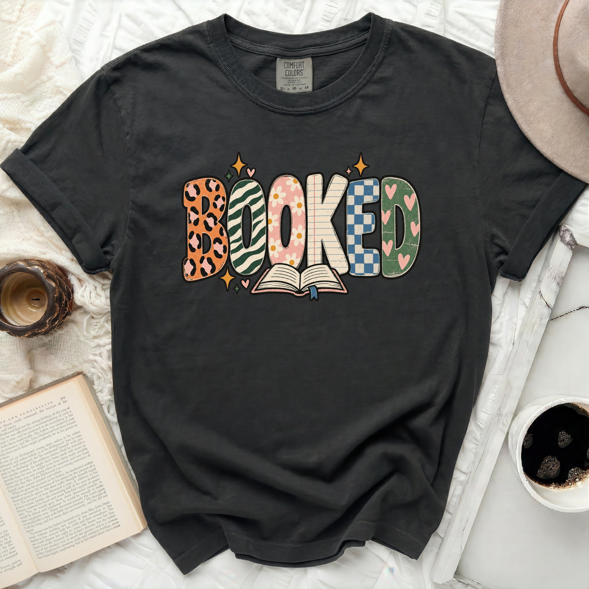 Dark gray t-shirt with "BOOKED" graphic featuring multiple patterns and an open book.