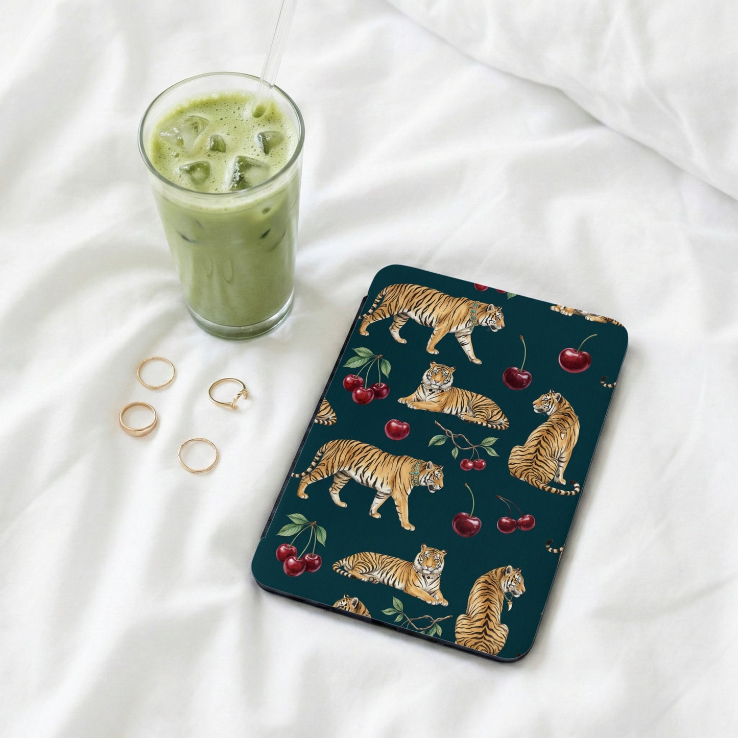Dark teal case with tiger and cherry pattern, next to a matcha latte and rings.