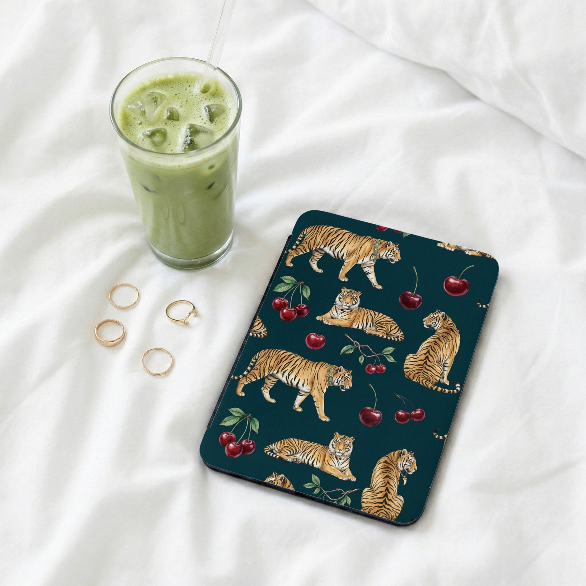 Dark teal case with tiger and cherry pattern, next to a matcha latte and rings.