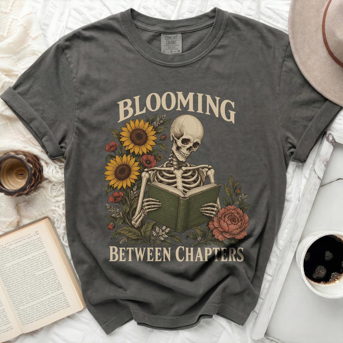 Skeleton reading book with sunflowers and roses, text "BLOOMING BETWEEN CHAPTERS".