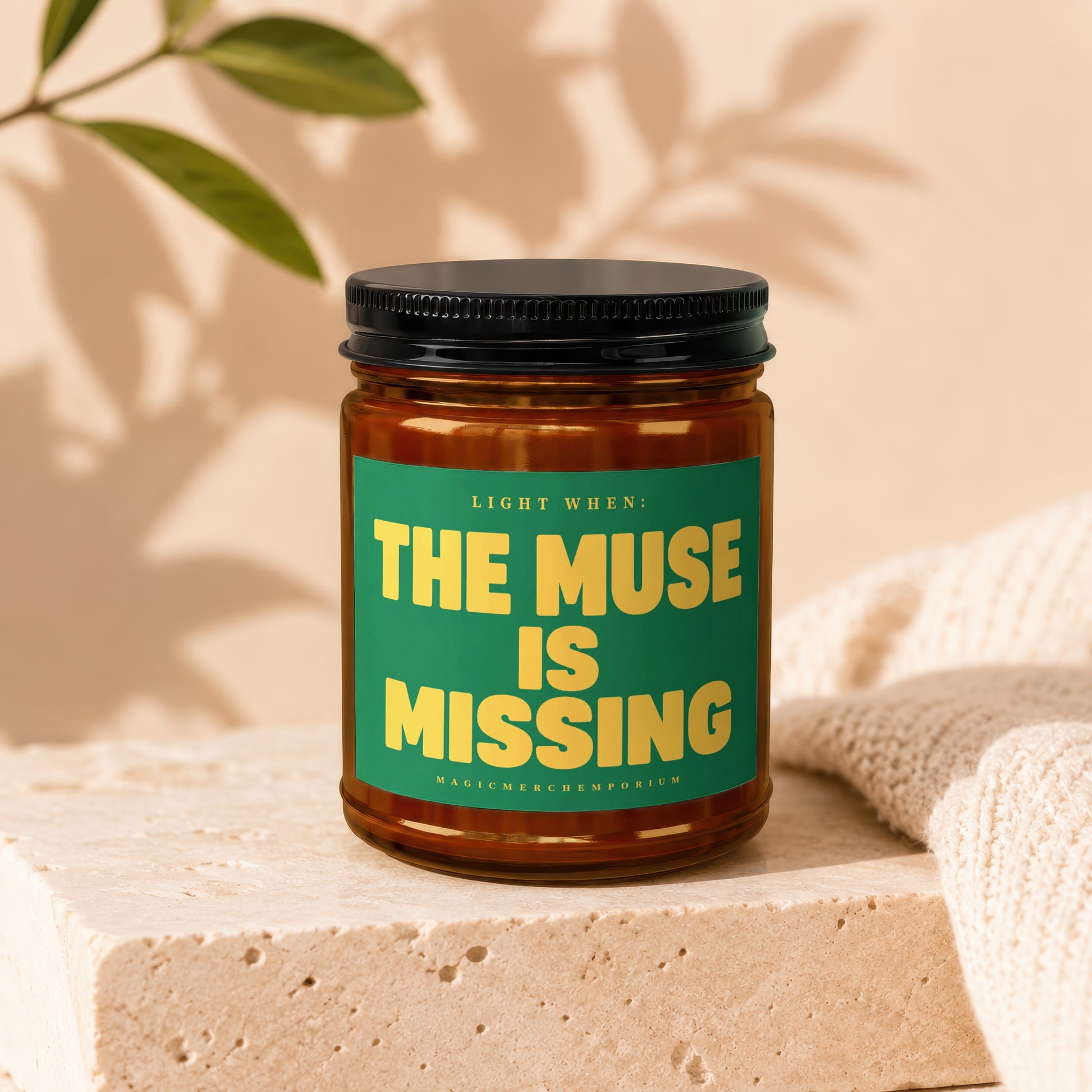 Amber glass candle with green label reading "LIGHT WHEN: THE MUSE IS MISSING"