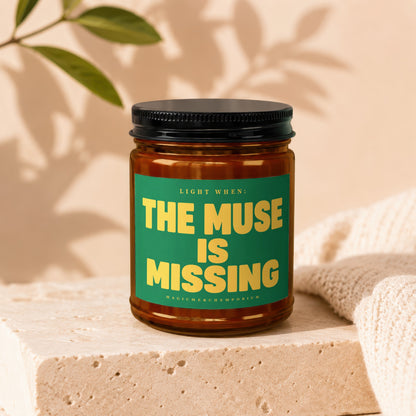 Amber glass candle with green label reading "LIGHT WHEN: THE MUSE IS MISSING"