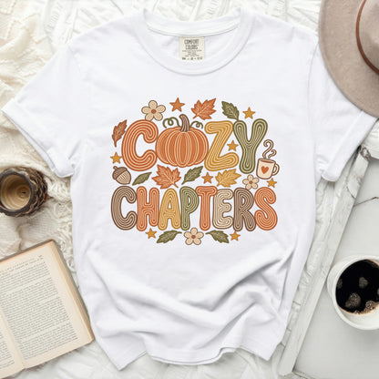 White t-shirt with "Cozy Chapters" text and autumn-themed graphics.