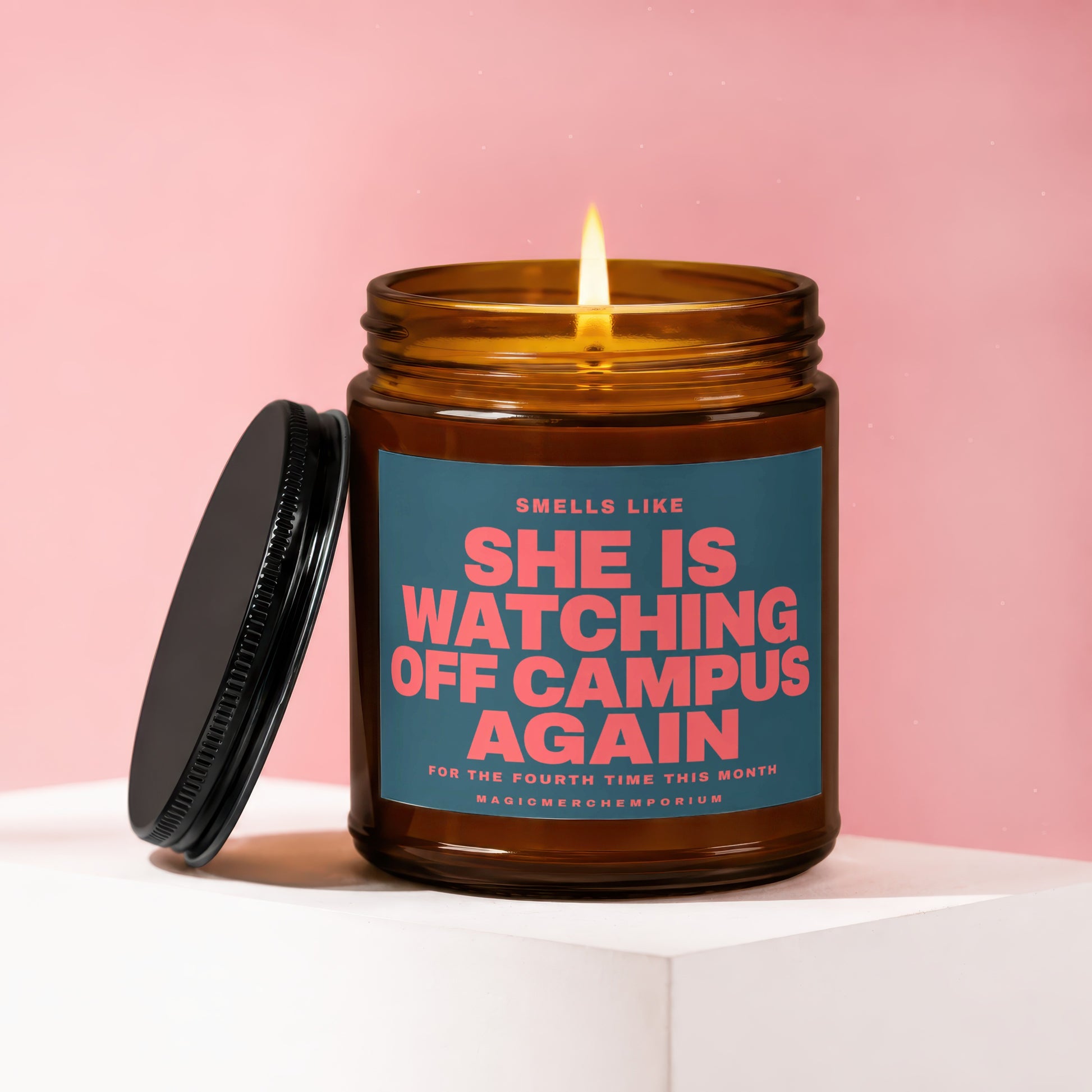 Amber jar candle with lit flame, reads "She is watching off campus again".
