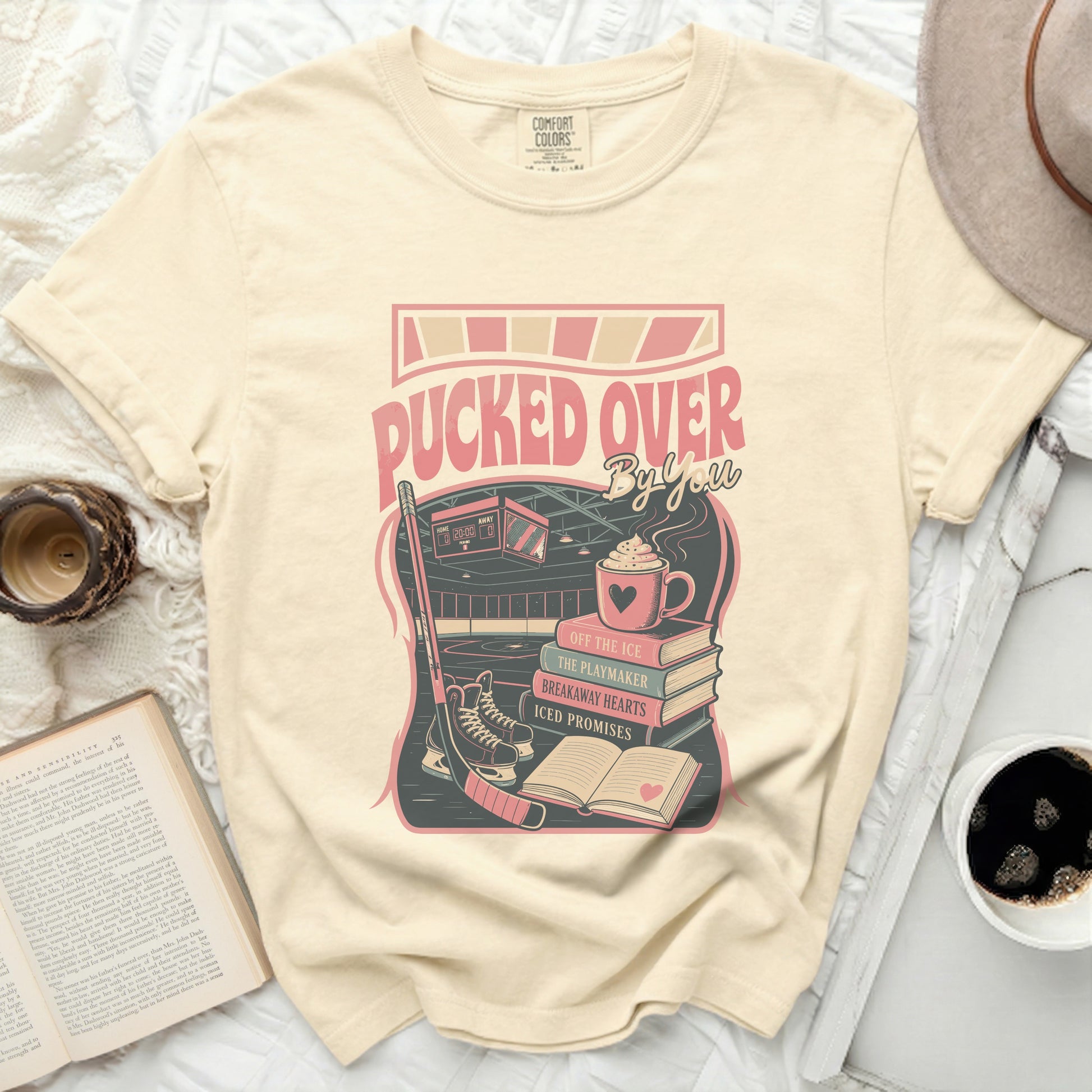 Cream t-shirt with "Pucked Over" graphic, hockey gear, and book titles.