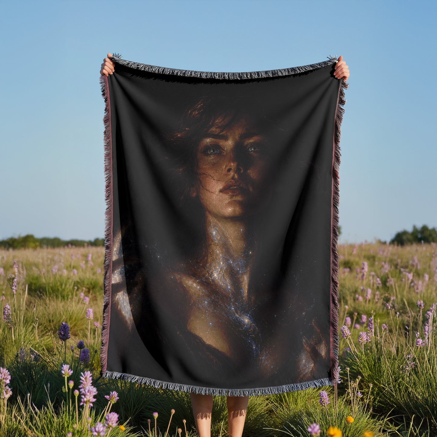 A person is holding a black blanket with a portrait of a woman printed on it, standing in a field of purple flowers.